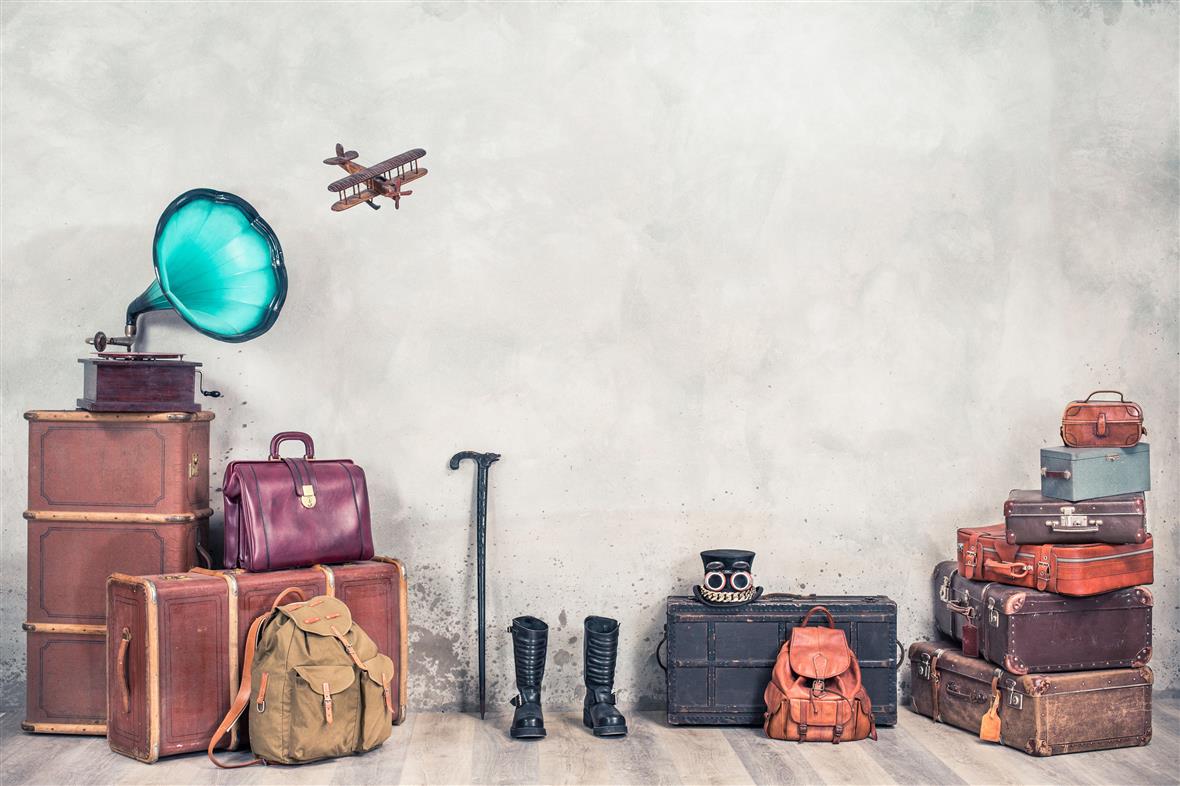 Vintage classic antique suitcases, old trunk luggage, backpack, leather boots, cylinder hat, gramophone and toy plane front concrete wall background. Travel baggage concept. Retro style filtered photo